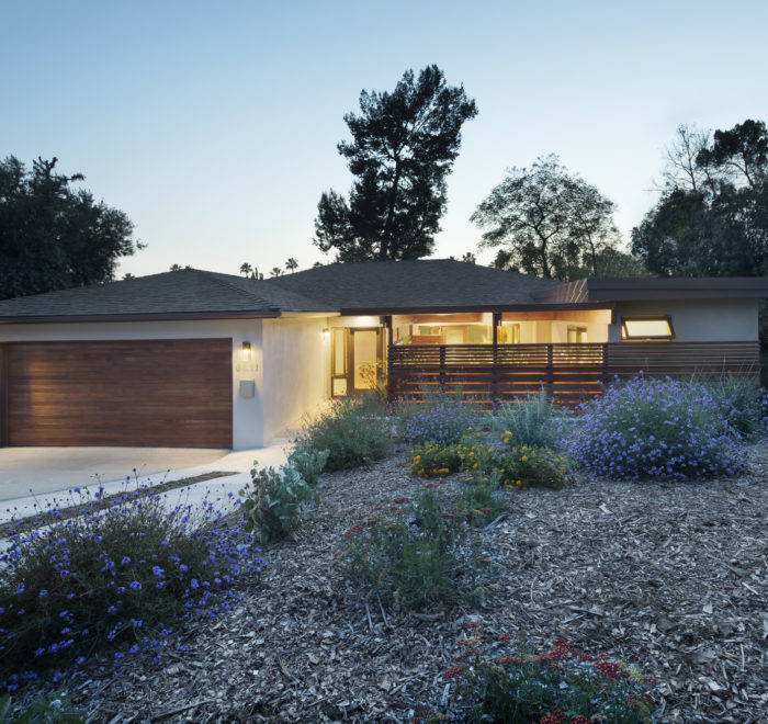 Photo of front facade of a modern house. Shows the wooden garage door, driveway, main entrance, and a flowerbed with woodchips.