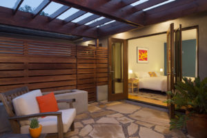 View of Bedroom from Private Outdoor of a modern house. Includes a wooden gate and overhead covering, a flagstone floor, a concrete fireplace, and a cushioned chair.