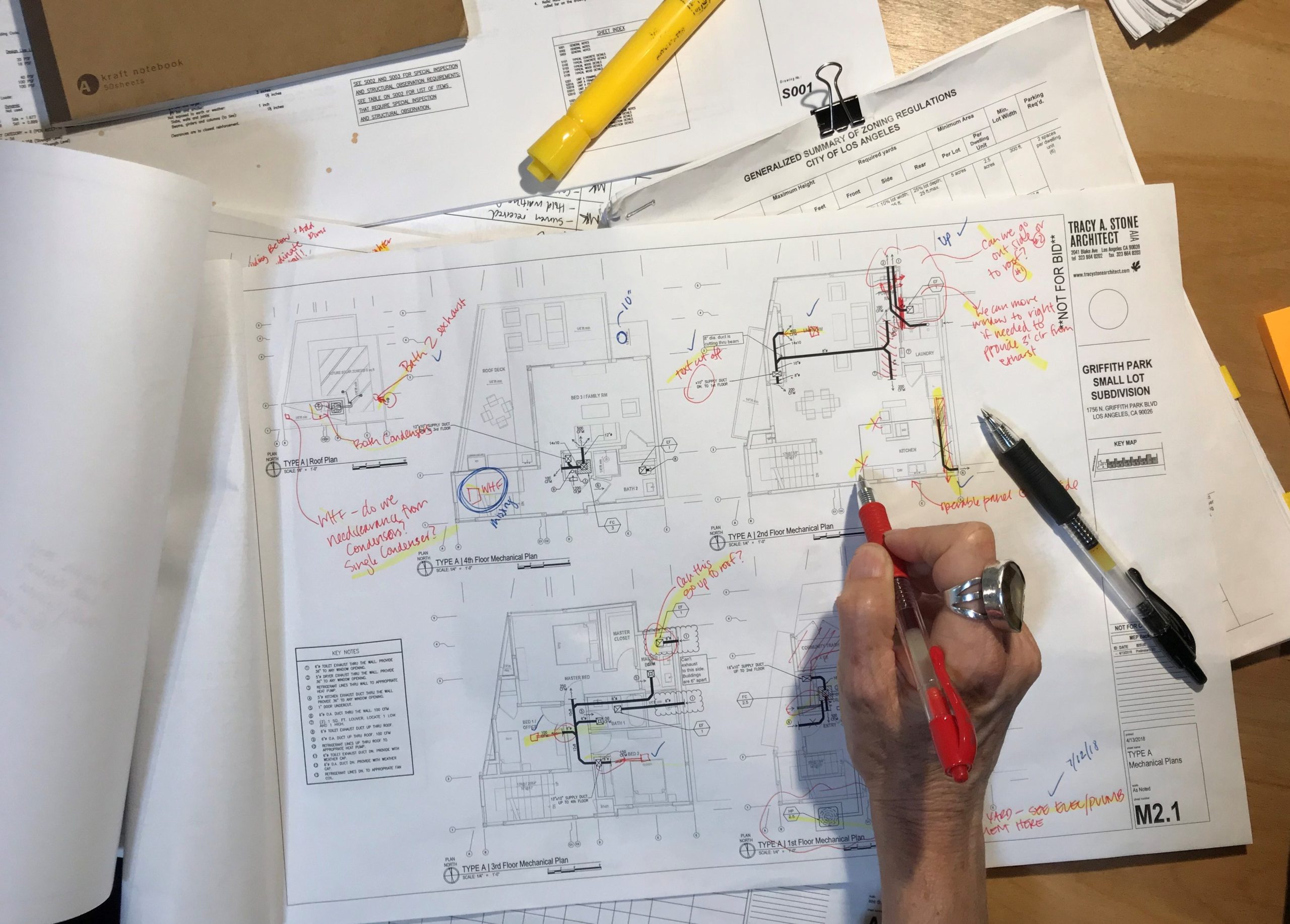 Photo of a hand holding a red pen, about to write on a set of marked up mechanical drawings.