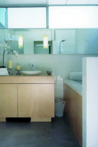 Photo of a bathroom and bedroom within a modern house. Features a wooden counter, a white tile sink, a concrete floor, and a large glass mirror.