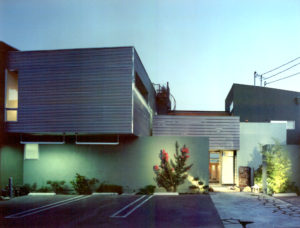 Photo of front entry for a modern house unit. Features a grooved upstairs, light green walls, and a view of the entryway and parking lot.