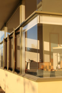 View of a modern building's corner connection in the sunlight. Includes the window framing and a peak into an interior bedroom.