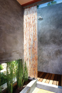 View of shower and skylight in a modern house. Shows concrete walls, wooden slatted floors, and plants lining the sides of the walls.