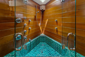 Photo of a shower within a modern house. Features wooden walls, blue tile floors, and double glass doors opening towards the viewer.