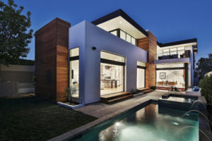 Photo of backyard and pool of a modern house. Includes white walls, turfstone pavers. and a look into the kitchen and living room through an open sliding glass door.