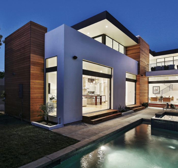 Photo of backyard and pool of a modern house. Includes white walls, turfstone pavers. and a look into the kitchen and living room through an open sliding glass door.