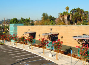 Photo of front of North Central Animal Services Center. Includes blue glass windows, a wooden and dark green stucco facade, and multiple flower trees lining the sidewalk.