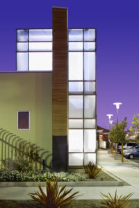 Rendering of the North Central Animal Services glass exterior. The lit up interior creates a white glow that shines against the wood and yellow plaster wall, as well as the purple sky.