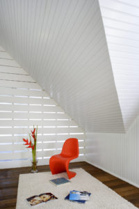 Interior photo of a vintage Los Angeles carriage house transformed to modern interior. Features white walls, a dark brown wood floor, and a neon orange chair on a white carpet.