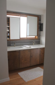 Photo of a custom mirror created for a modern house. The mirror features two different panels above two separate sinks, and sits within a wooden frame at offset levels.