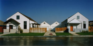 Photo of two four modern houses from across the street. A red wagon lies in the driveway, with two houses on either side.