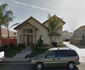 Photo of an older house within a suburban neighborhood. The house has Spanish tile roof, beige walls, and two trees in the front yard.