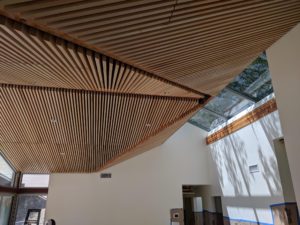 Photo of a wood slat ceiling and skylight for a modern house during construction. The ceiling and skylight cover the top half of the image, while a white stucco wall cover the bottom half.