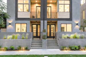 Photo of the front entry for a modern townhouse. Shows the entry door, balcony, concrete and wood exterior walls, and concrete planters.