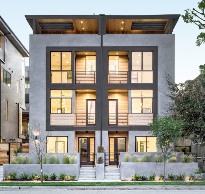 Photo of the front facade for a modern townhouse. Shows the entry door, multiple balconies, rooftop space, and concrete and wood exterior walls.