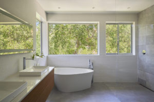 View of a modern bathroom. Includes a bathtub in the corner, an open concept shower separated by a glass partition, and a wooden counter with a marble countertop.