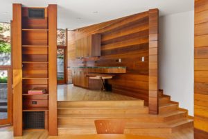 View of kitchen within a modern house. Includes a white stucco ceiling, wood floors and walls, wood storage units, and wood furniture.