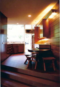 View of a kitchen within a modern house. Features a red tile floor, wood walls, wooden cabinetry, and wooden furniture.