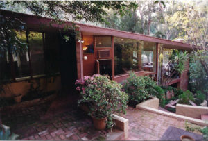 View of front entrance of a modern house. Shows the wood walls and roof, multiple doors to different areas of the house, and glass windows along the entire front facade.