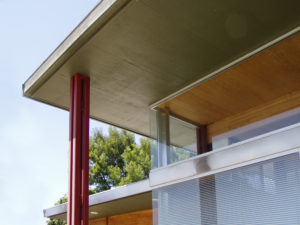 View of Building Corner for an office building. Shows exterior roof that overhangs the interior of the space, as well as a metal red column coming down from the exterior roof.