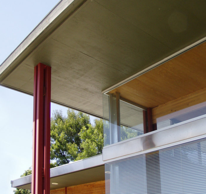 View of Building Corner for an office building. Shows exterior roof that overhangs the interior of the space, as well as a metal red column coming down from the exterior roof.