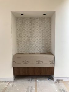 Photo of construction of a counter embedded into a white plaster wall within a modern house. The wood counter is covered with cardboard and sits against tile.