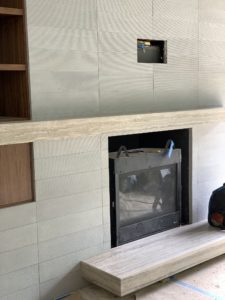 Construction photo showing the installation of a fireplace into a gray brick wall.