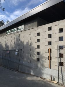 Photo showing construction of the exterior facade of a modern house. A chainlink fence leans against a protruded gray block wall.