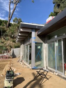 Construction photo showing work on the back exterior facade and the pool. Blue tape is marked against the windows, while machinery and materials are strewn across the ground.