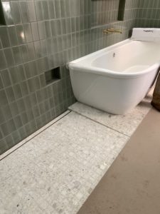 Picture of the construction of the bathroom of a modern house. The white bathtub sits on top of white marble, while the green tile walls have indents for storage.