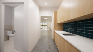 Photo of kitchen area leading into the main space. The kitchen features wooden cabinets and a marble countertop against blue tile, while a separate door to the left leads into the restroom.