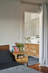 Photo of a bedroom and bathroom within a modern house. Includes wood floors and white plaster walls in the bedroom, blue tile floors and white marble walls in the bathroom, and a curtain that divides the two rooms.