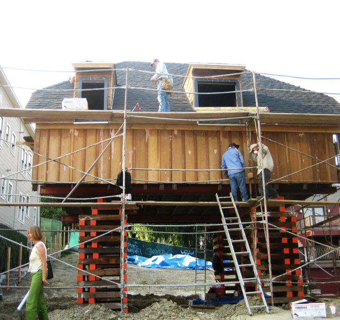 Photo of construction work on the second floor of a modern house. With no first floor present, wooden turning blanks are stacked to hoist the second floor of the building above the ground