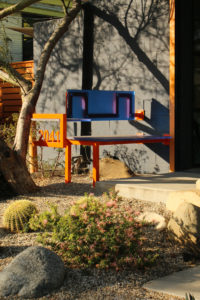 View of orange steel tubes and blue plastic panels, featuring an orange steel address number welded to the side.