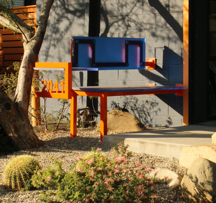 View of orange steel tubes and blue plastic panels, featuring an orange steel address number welded to the side.