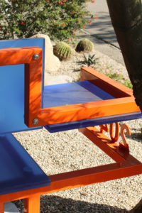 Closeup of orange steel tubes and blue plastic panels, featuring an orange steel address number welded to the side.