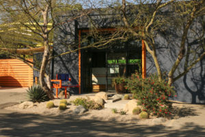 Wide shot of office entrance and orange steel tubes and blue plastic panels, featuring an orange steel address number welded to the side.