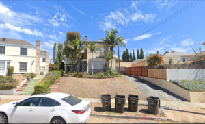 View of an existing vacant triplex surrounded by suburban houses from the street.